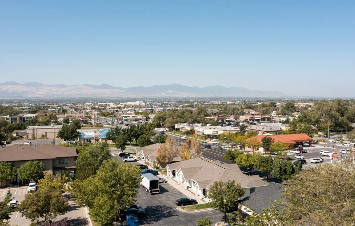 Expansive aerial perspective showcasing a community with varied architectural styles, mature trees, and mountainous terrain in the distance