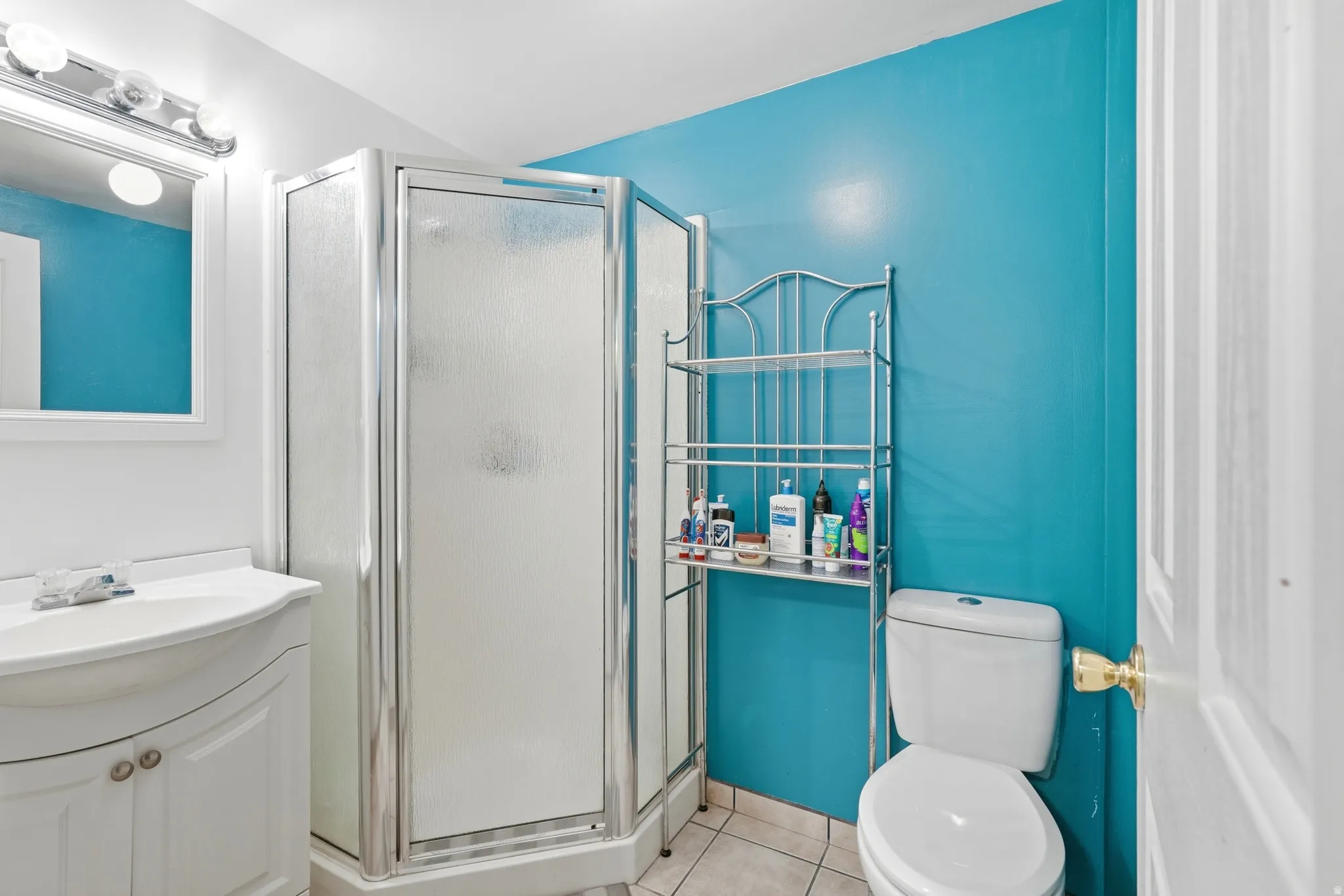 Bathroom featuring a corner shower enclosure with frosted glass panels, a white vanity with integrated sink, and tiled flooring
