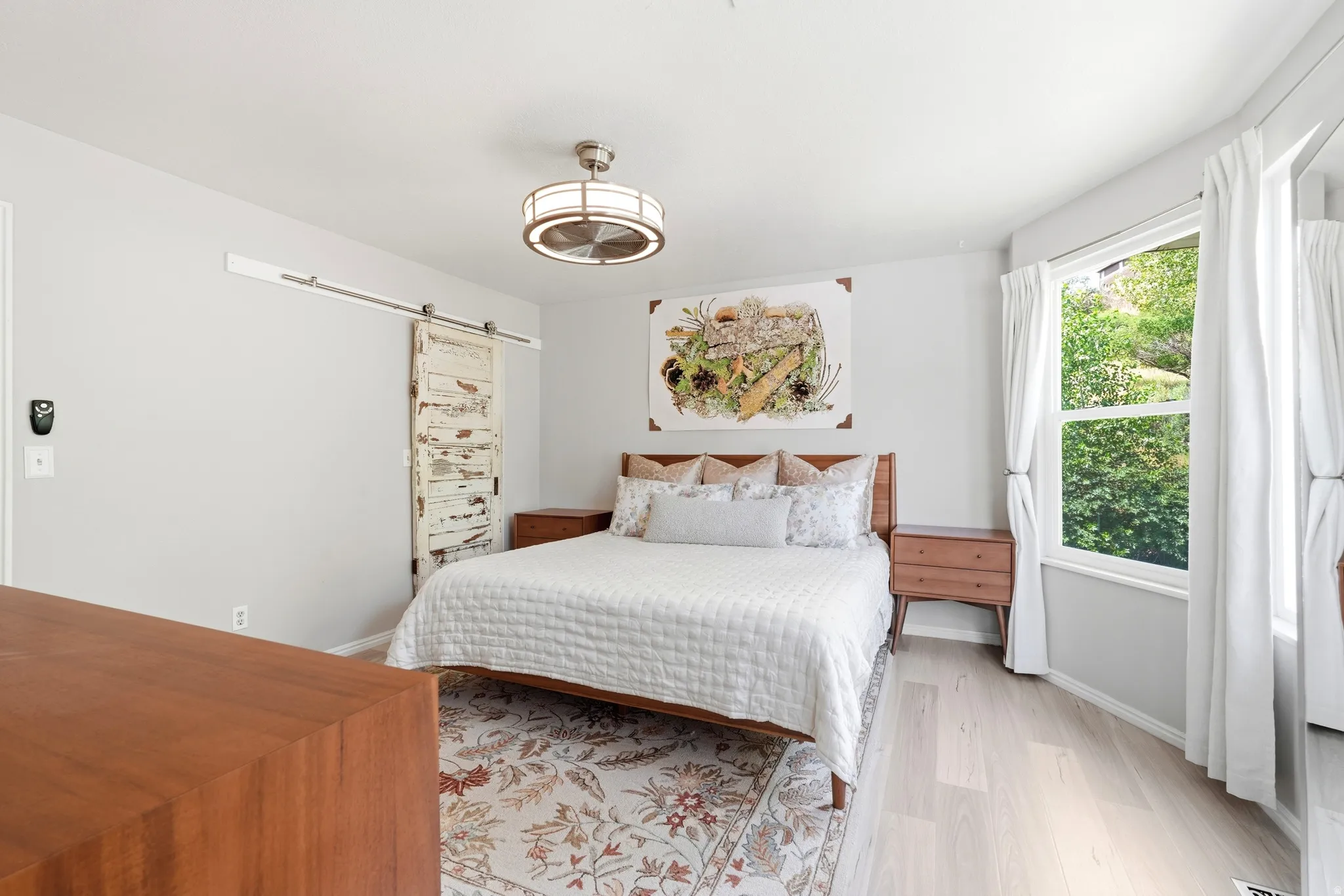LVP flooring with a decorative area rug, a built-in window, a distressed sliding barn door, and a modern ceiling fan with integrated lighting