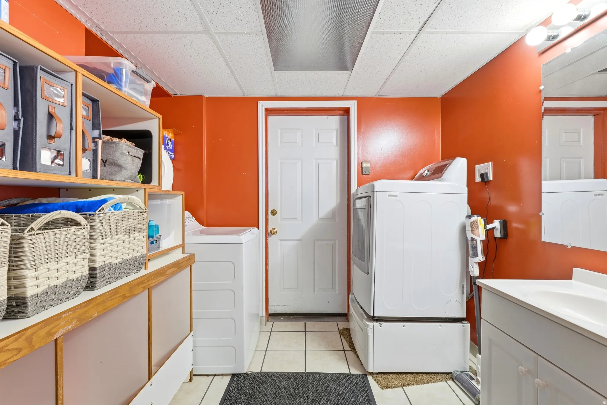 Laundry room with tile flooring, built-in shelving, white paneled door, and a vanity with an integrated sink