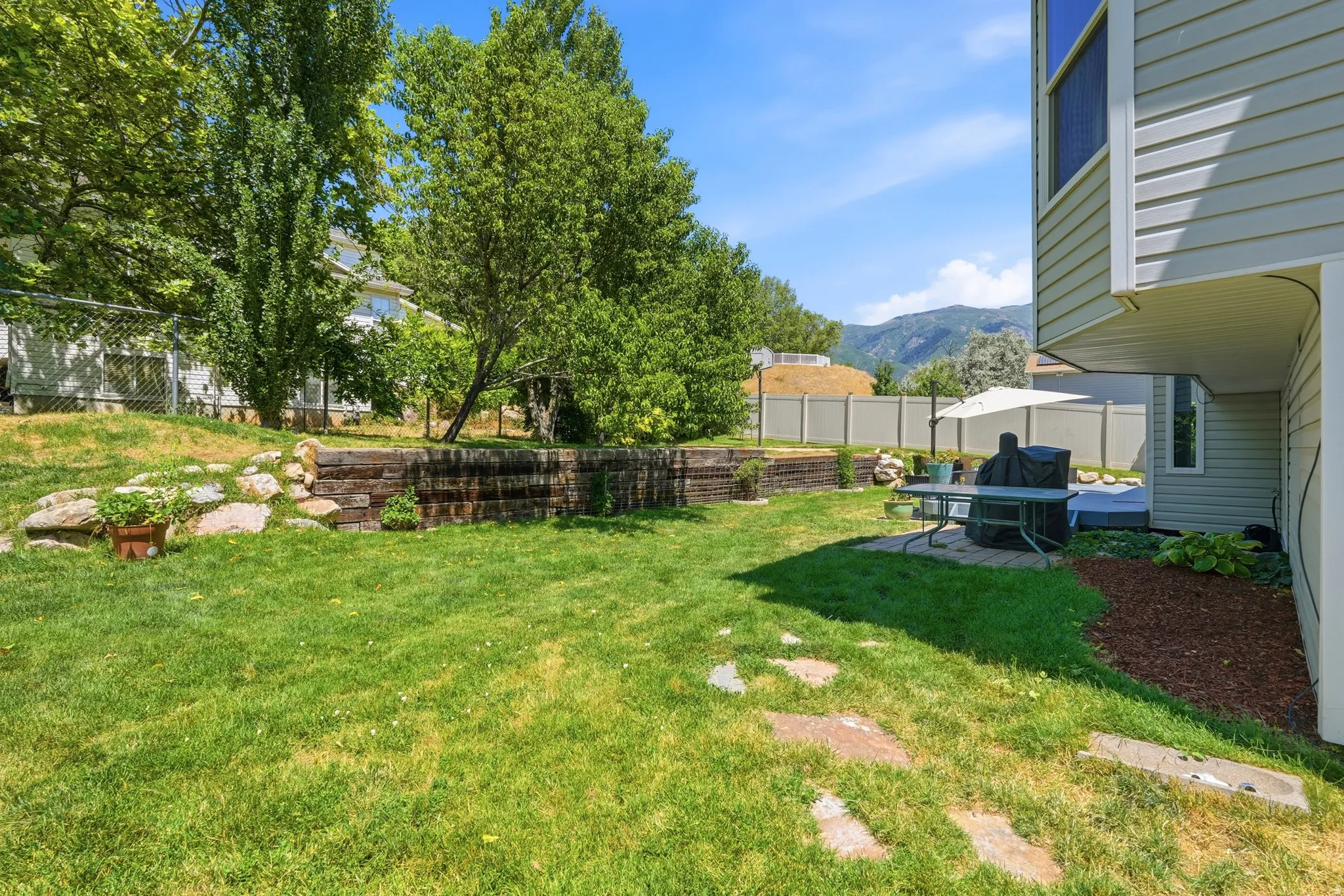 Expansive backyard featuring a manicured lawn, stone paver pathway, and a patio area with a privacy fence