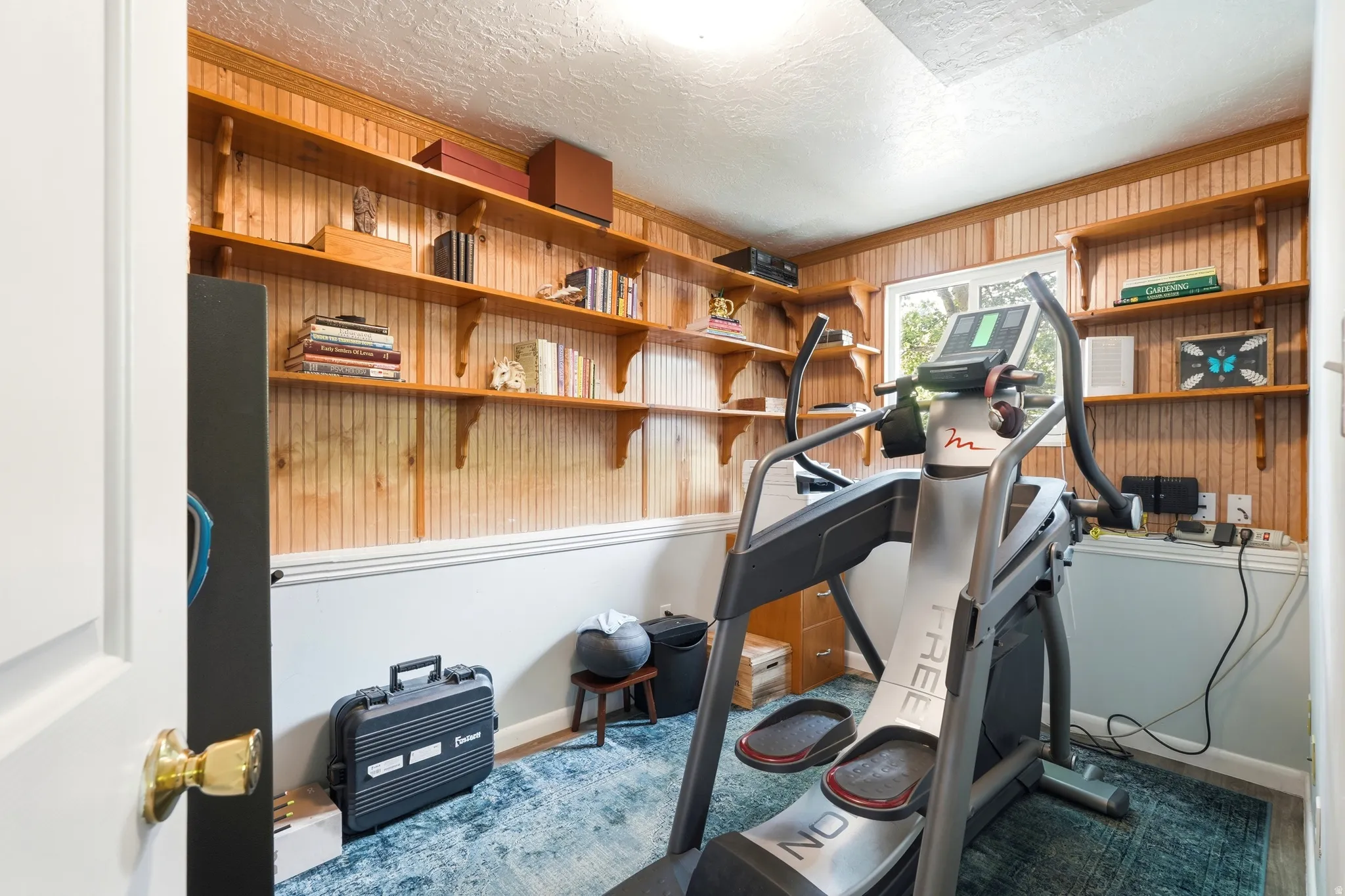 Room featuring extensive built-in wooden shelving, beadboard paneling, a single window, and painted wainscoting