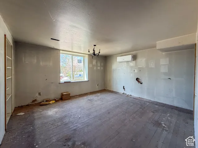 Expansive room with wood plank flooring, a large window, built-in shelving, and a wall-mounted mini-split system