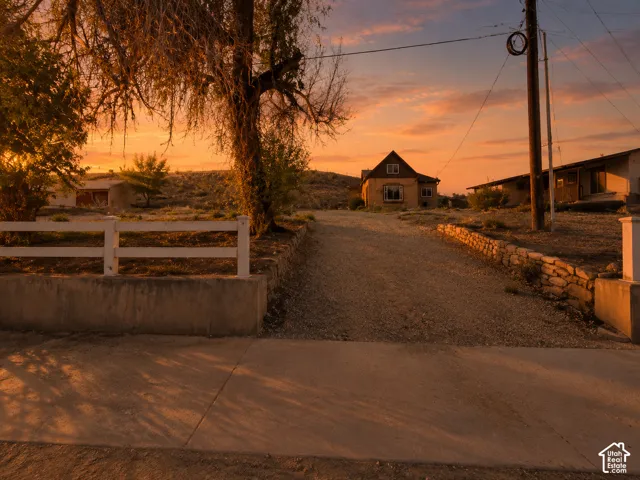 Gravel driveway leading to a residence featuring a stone retaining wall and a white fence