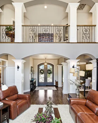 Grand Great Room with Soaring Ceilings and Striking Architecture Featuring a Second-Story Overlook with Iron Balusters and White Columns