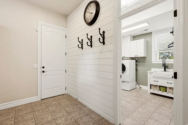 Practical Utility Room/Mud Room with Shiplap Accent Wall, Tile Flooring, and a Plethera of Storage with a Pocket Door Leading to the Spacious Laundry Room and White Arched-Panel Door Leading out to the Oversized 3-car Garage