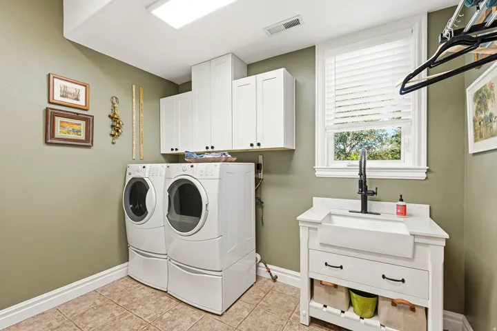 Dedicated Laundry Space Featuring White Shaker Cabinetry, Tiled Flooring, a Farmhouse Sink with a Black Gooseneck Faucet, and a Window for Natural Light