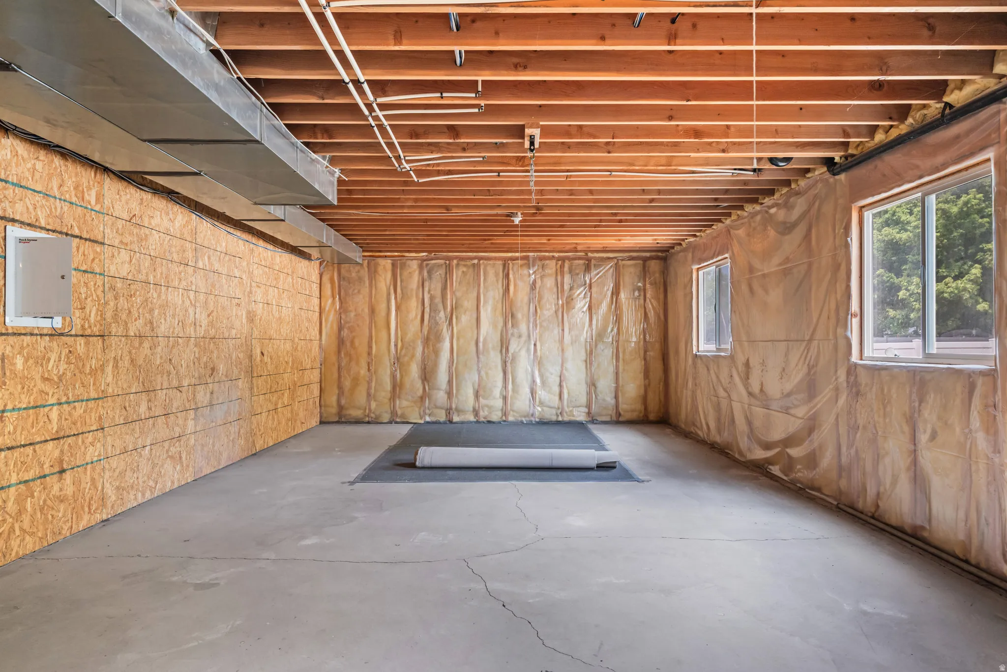 Unfinished basement featuring exposed wood joists, concrete flooring, and multiple windows