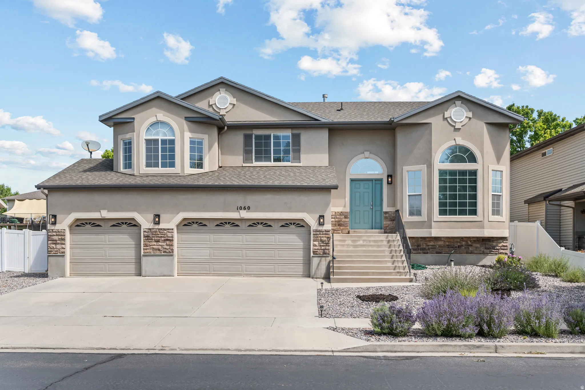Stucco exterior residence featuring a teal front door with an arched transom, a two-car garage, and a three-car driveway