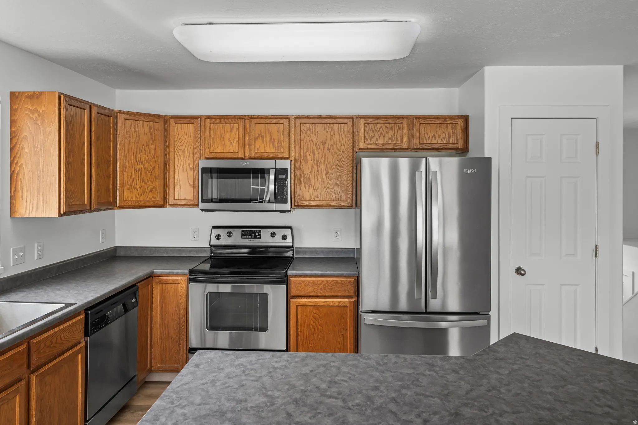 Kitchen featuring wood cabinetry, stainless steel appliances, dark countertops, and an integrated sink
