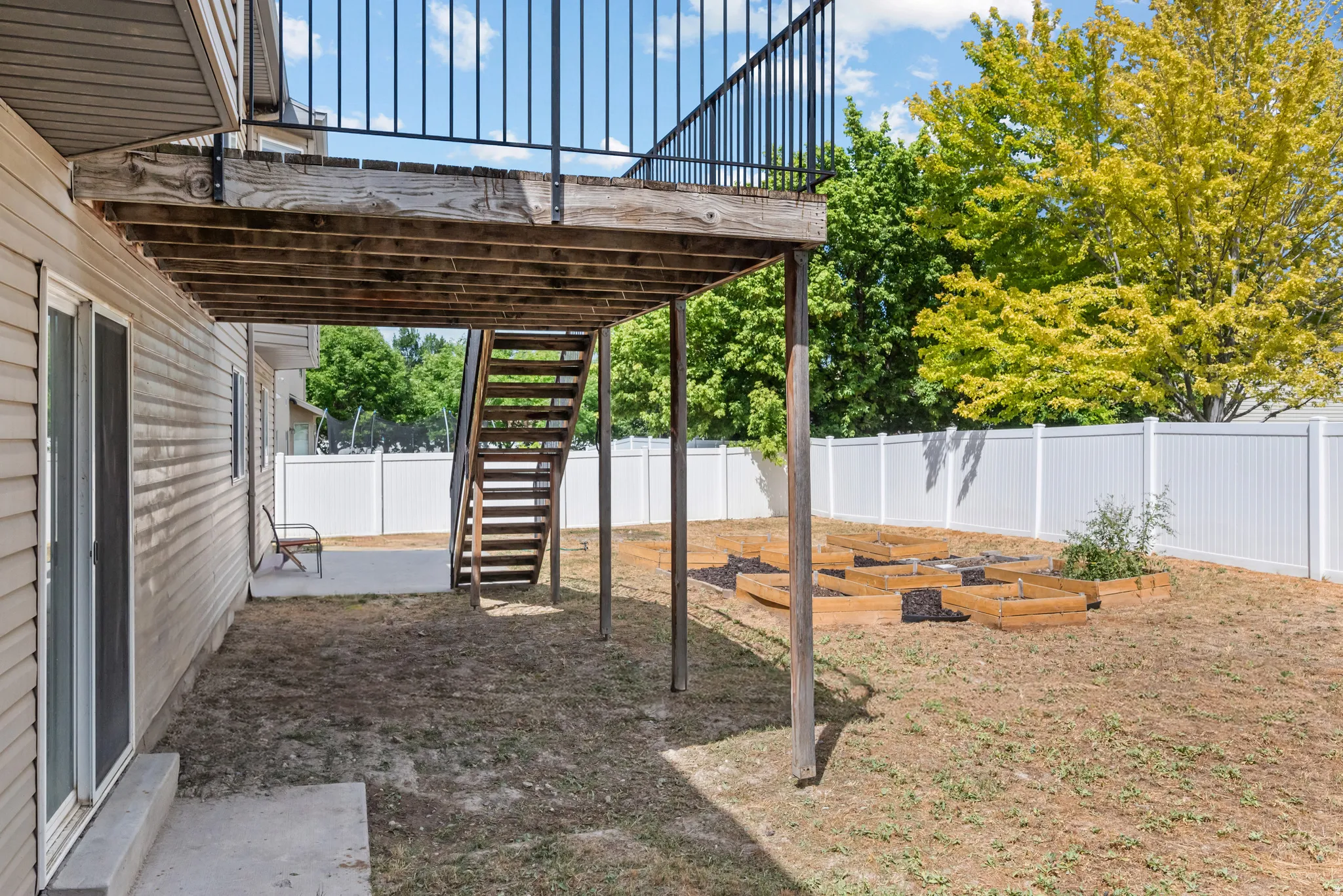Rear exterior featuring a raised wood deck with black metal railings, leading to a fenced backyard