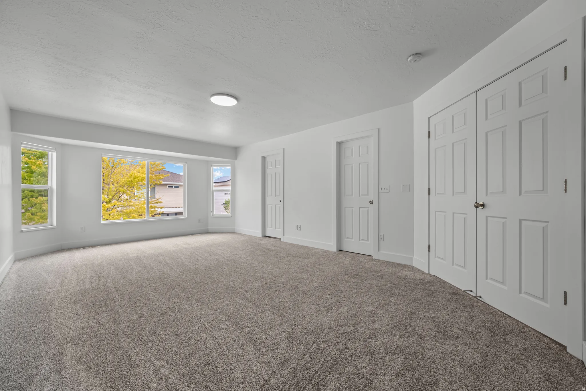 Spacious room featuring light gray carpet, multiple windows, white painted walls, and white paneled doors