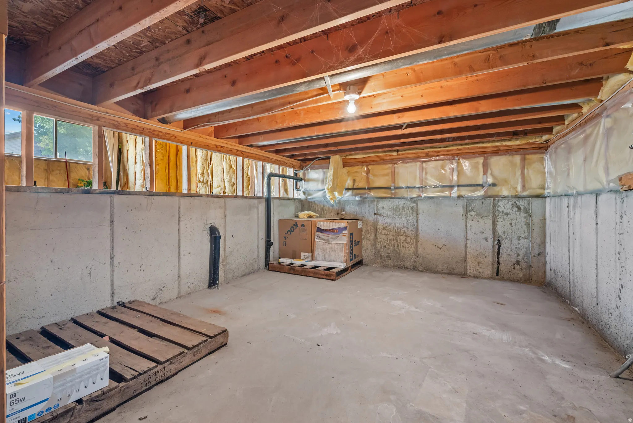 Unfinished basement space featuring exposed wooden ceiling joists, poured concrete walls, and a concrete floor