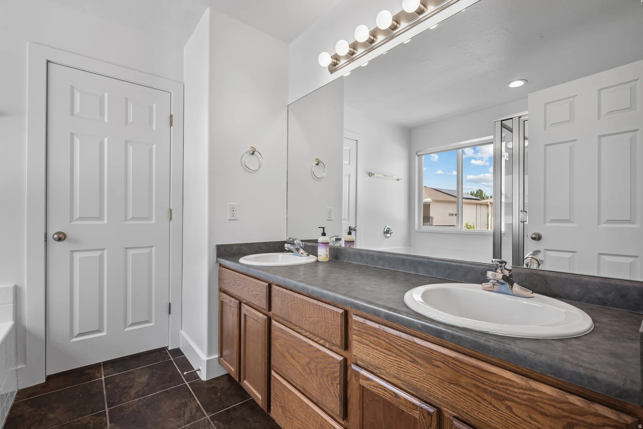 Double vanity with dark countertops and wood-finish cabinetry