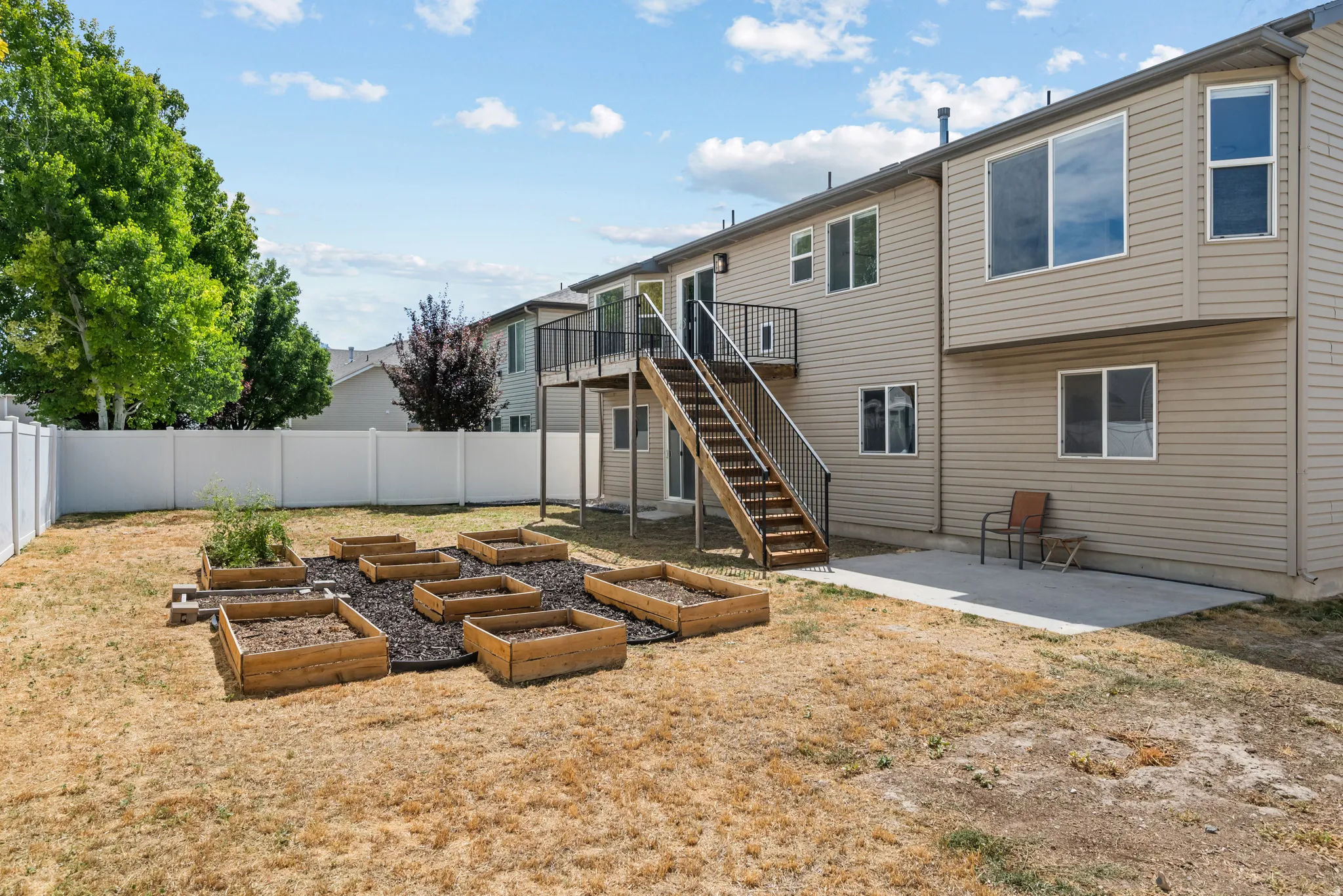 Expansive backyard featuring multiple raised garden beds, a privacy fence, and a concrete patio