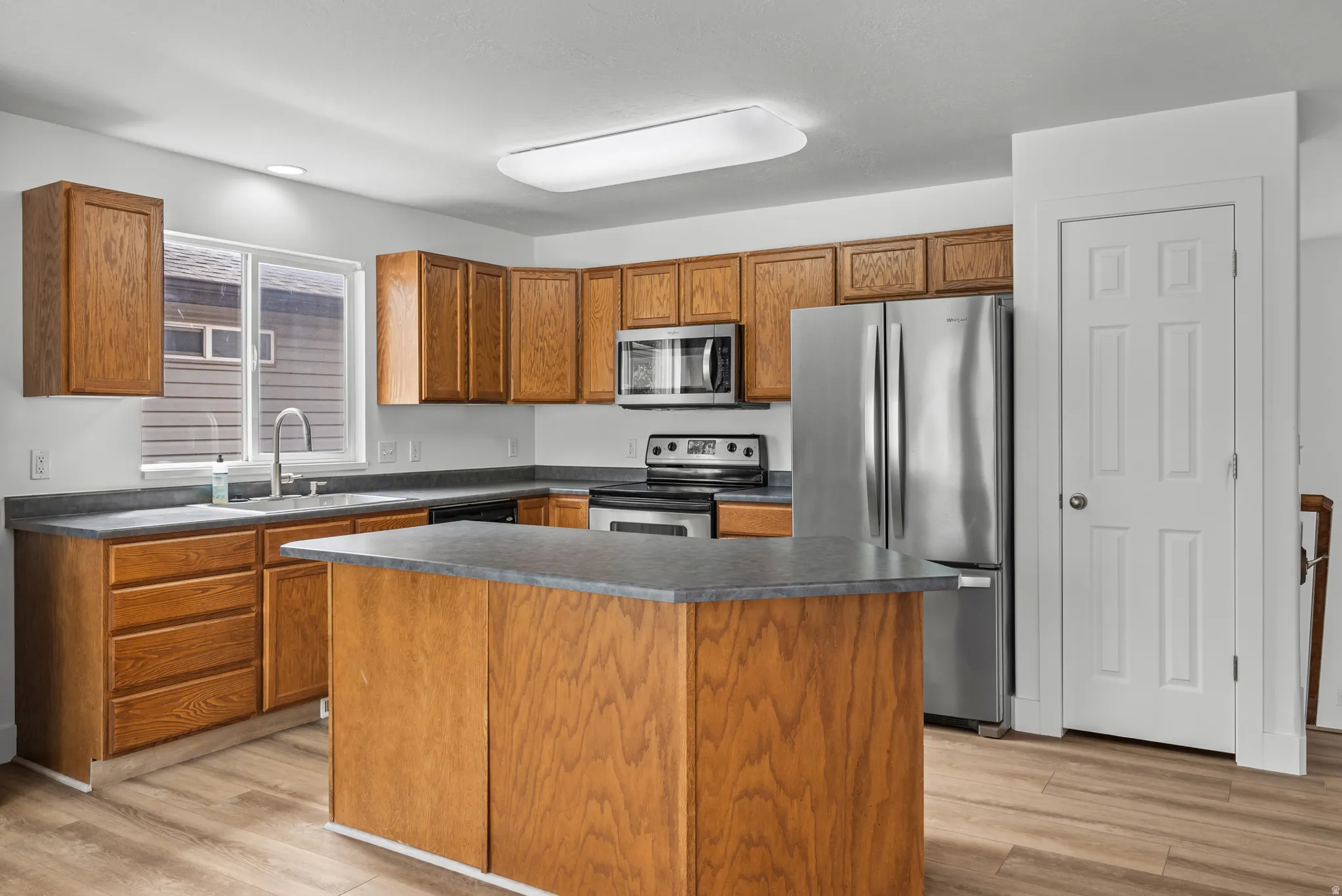Kitchen featuring wood-finish cabinetry, stainless steel appliances, a center island with countertop, a window above the sink, and wood-finish flooring