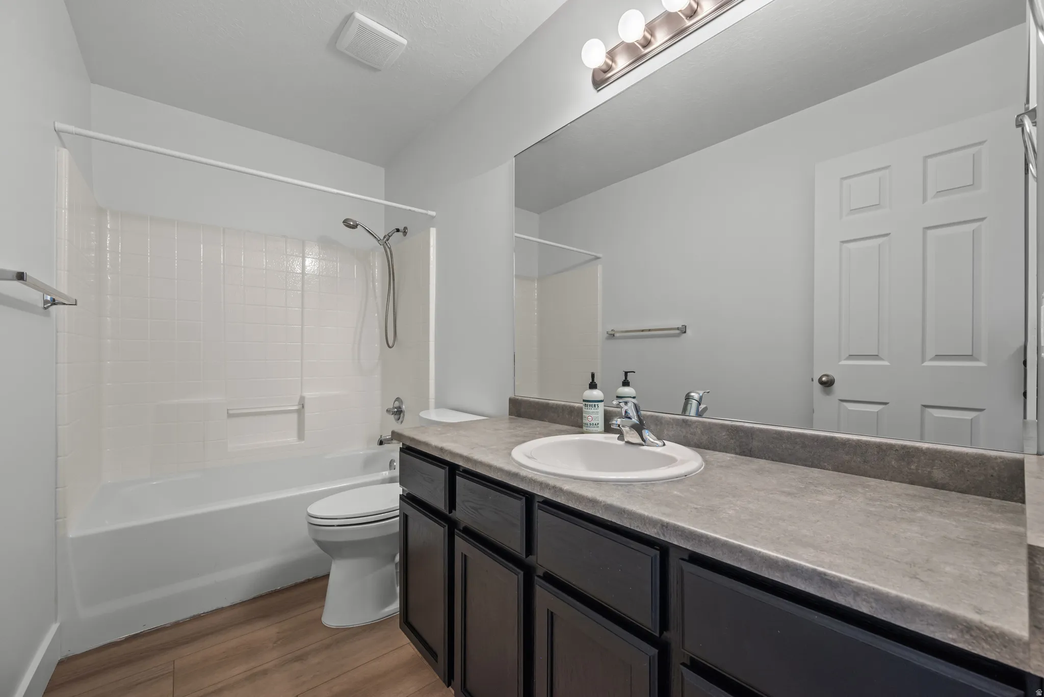 Bathroom featuring a full-width vanity with dark cabinetry, an integrated sink, and an expansive mirror