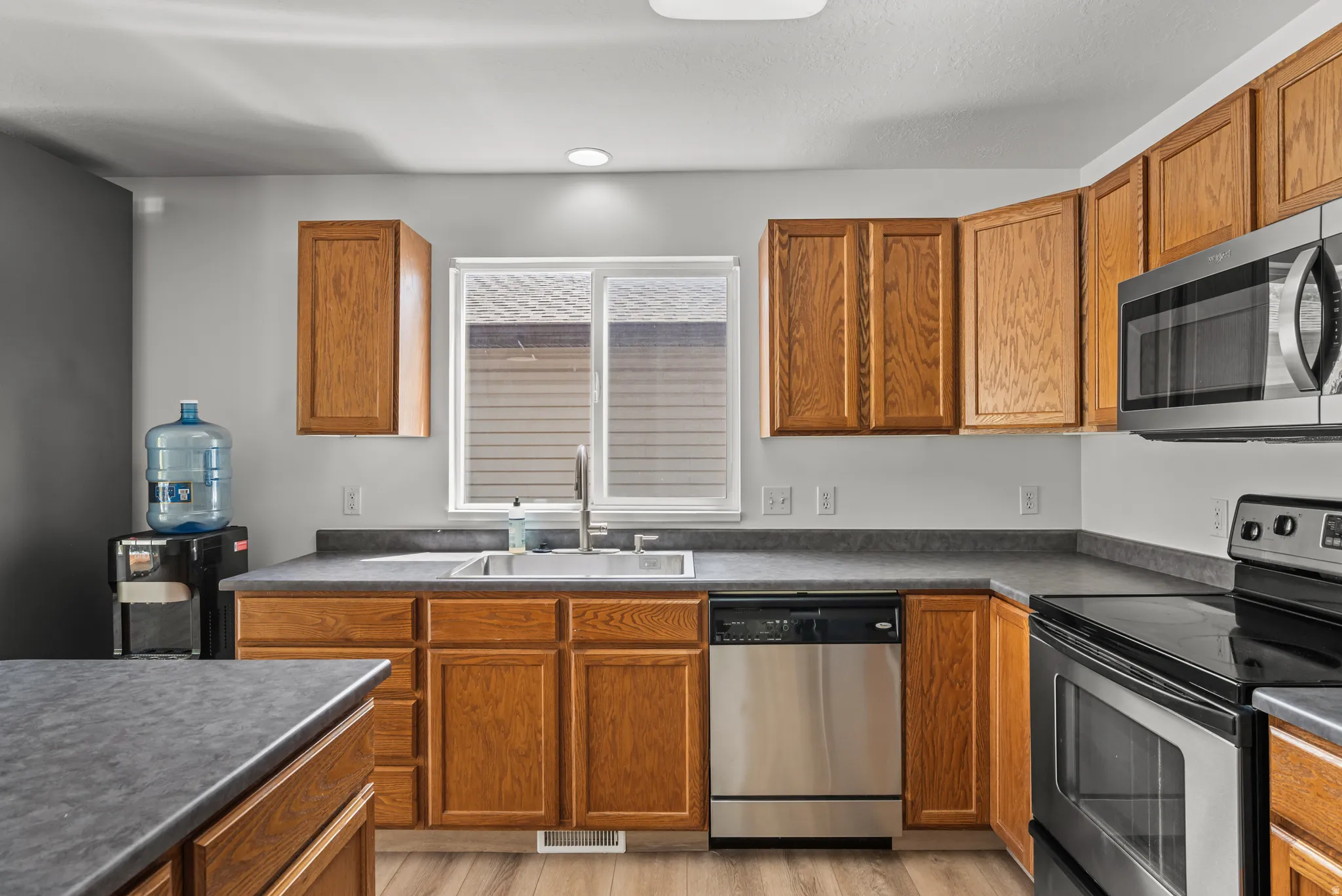 Kitchen featuring wood cabinetry, dark countertops, a stainless steel sink with a gooseneck faucet, a stainless steel dishwasher, and a stainless steel range with an over-the-range microwave