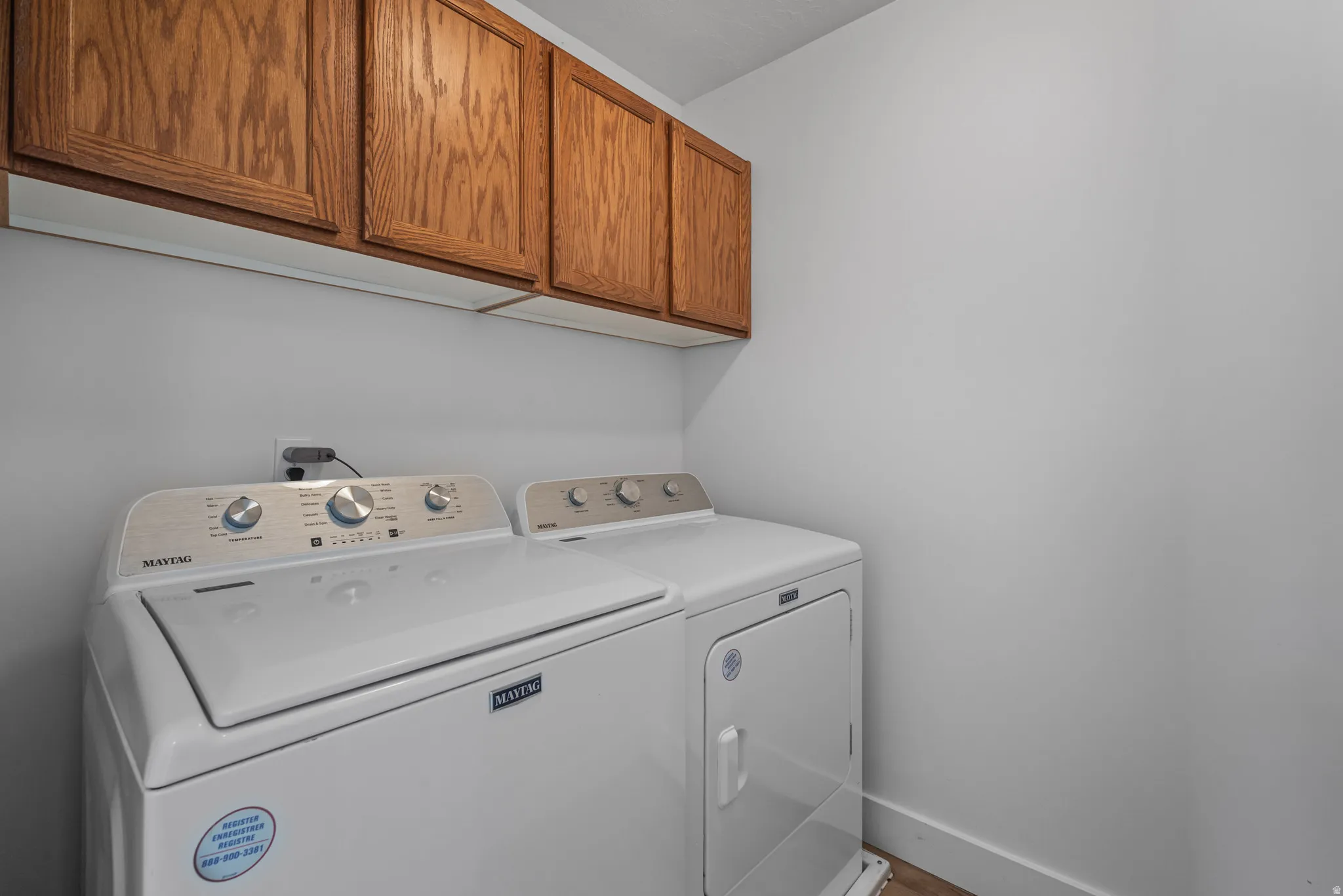 Dedicated laundry area featuring overhead wood-finish cabinetry and light-toned walls