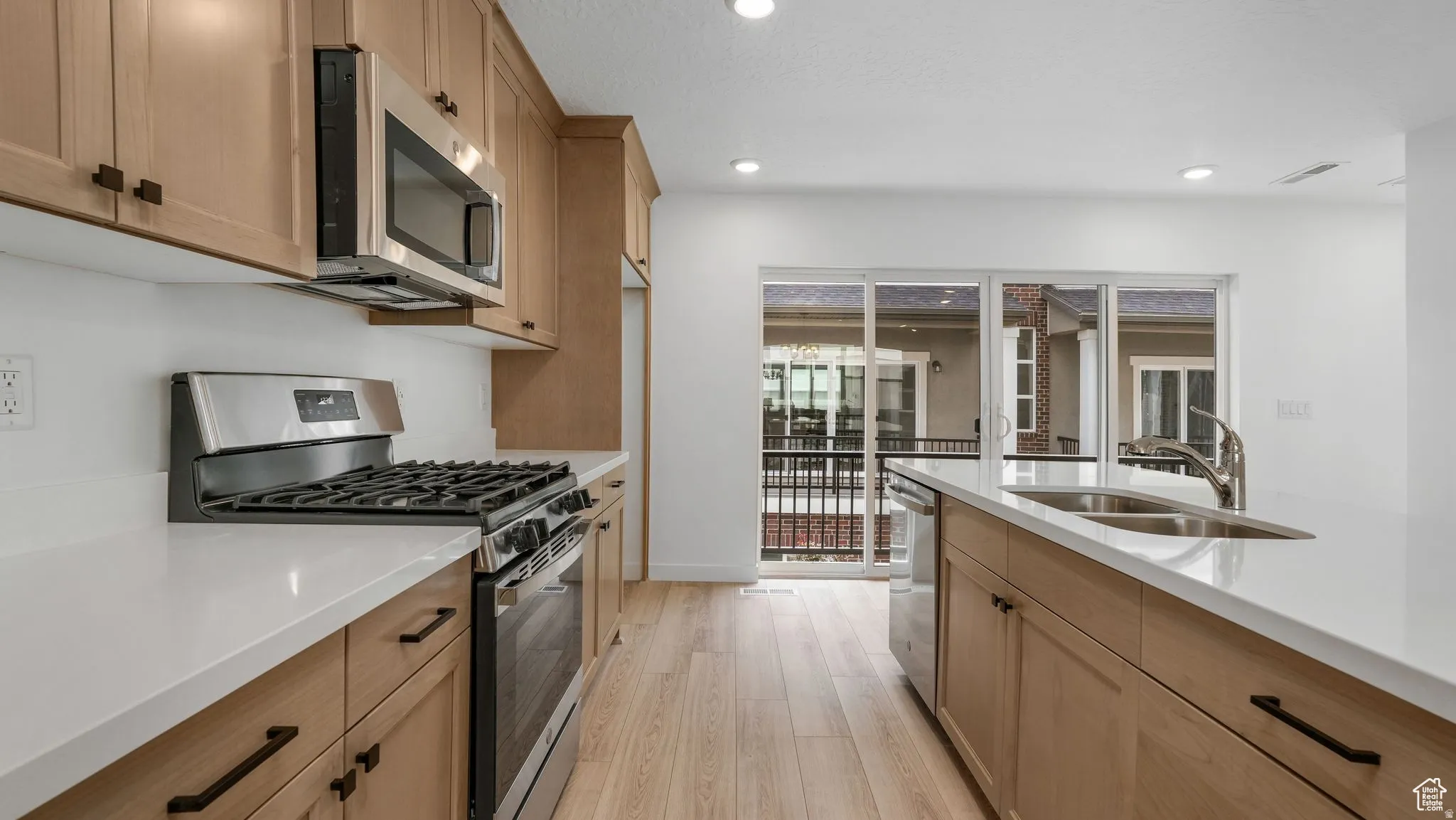 Modern kitchen featuring light wood-finish cabinetry with matte black hardware, stainless steel appliances, and white countertops
