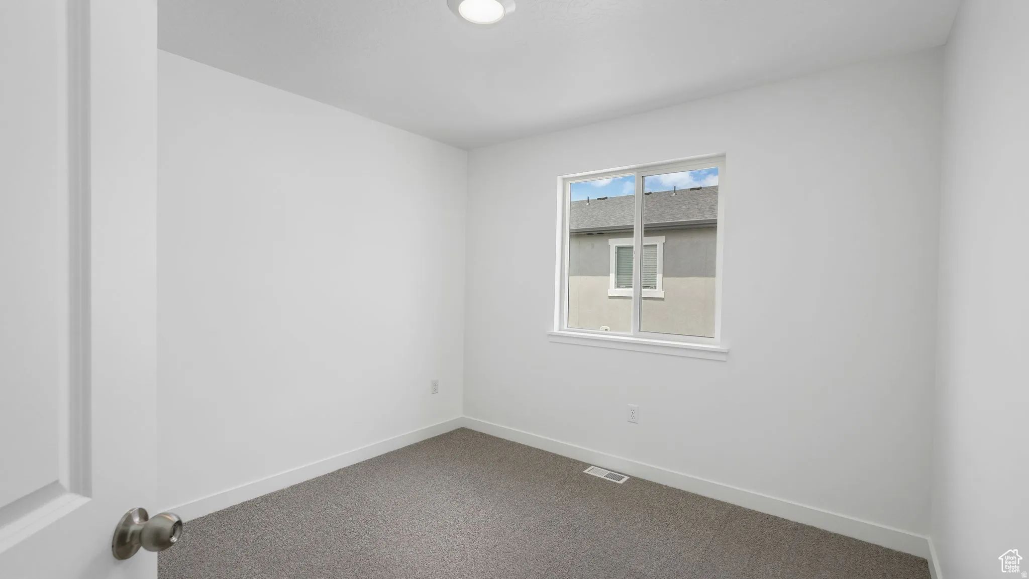 Neutral wall tones, gray carpet flooring, white trim, single window, and flush-mount ceiling light