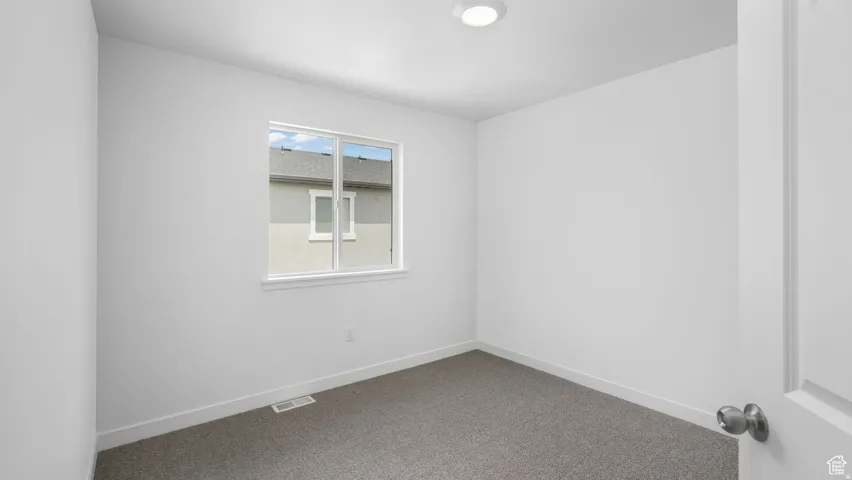 Neutral white walls throughout, showcasing a window with white trim, gray carpeting, and a recessed ceiling light fixture
