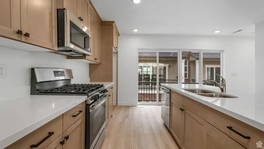 Modern kitchen featuring light wood-finish cabinetry with matte black hardware, stainless steel appliances, and white countertops