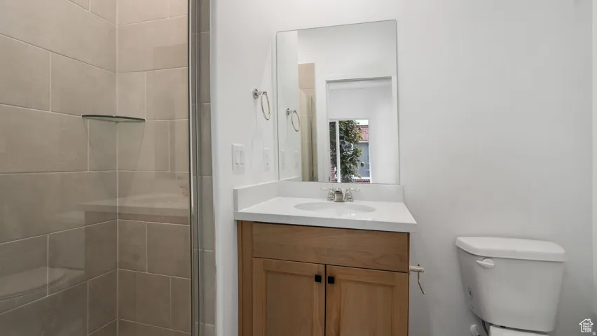 Bathroom featuring a glass-enclosed shower, light-toned tile, a floating corner shelf, and a vanity with a white countertop