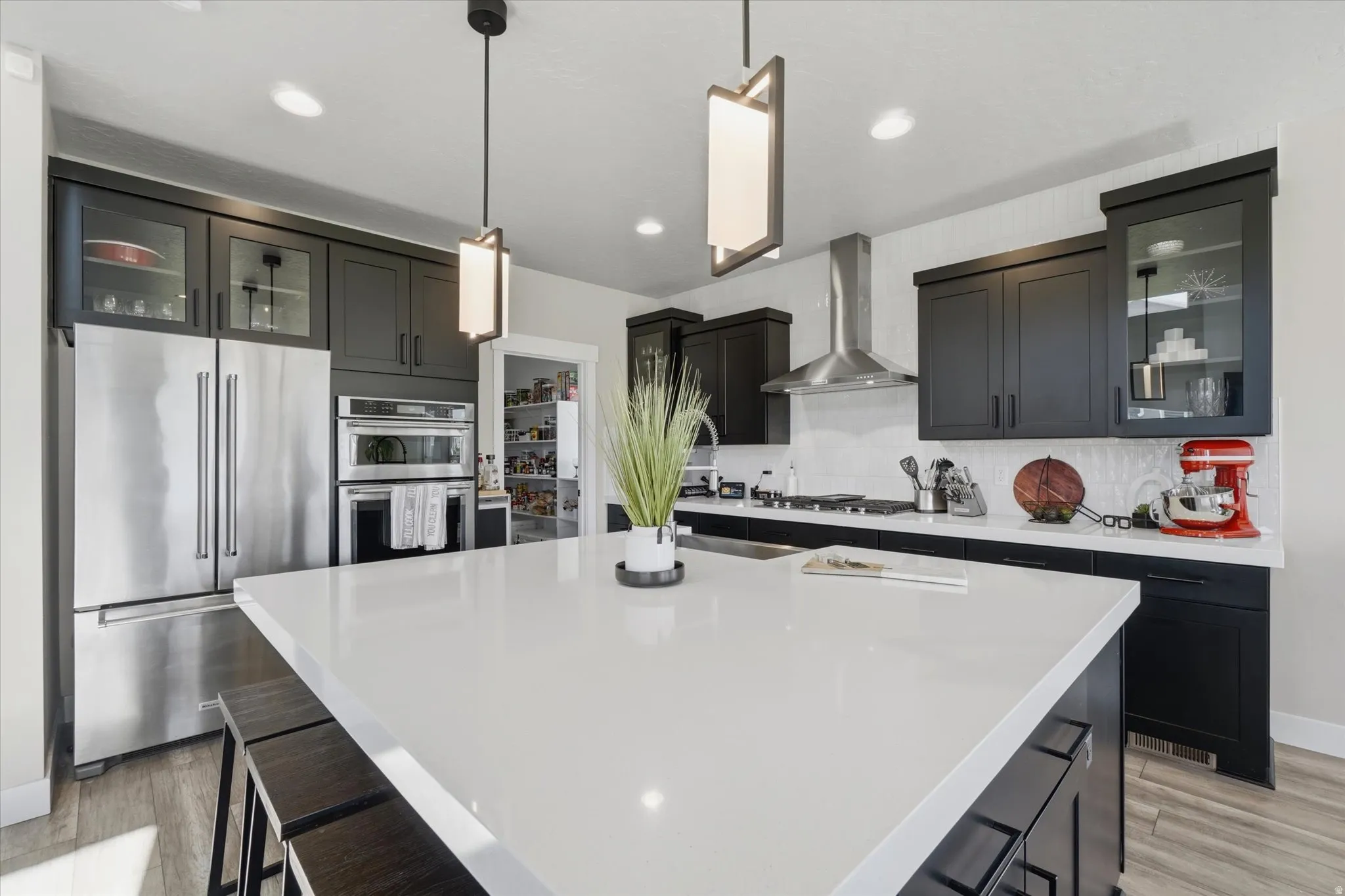 Spacious kitchen featuring a large central island with a white solid surface countertop, dark wood-finish flooring, recessed lighting, and modern pendant fixtures