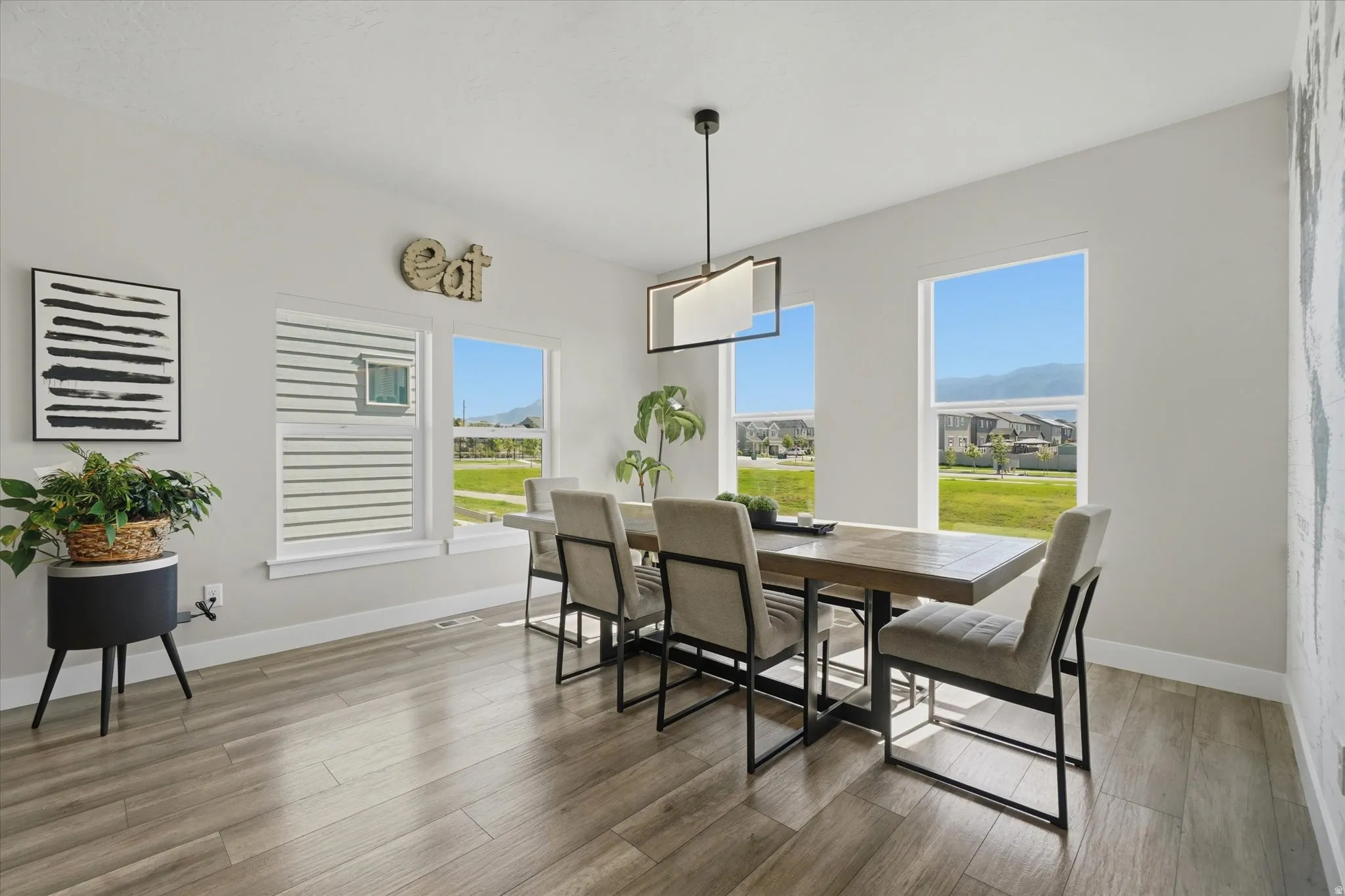Well-lit dining area featuring wood-finish flooring, multiple windows providing abundant natural light, and a modern rectangular chandelier