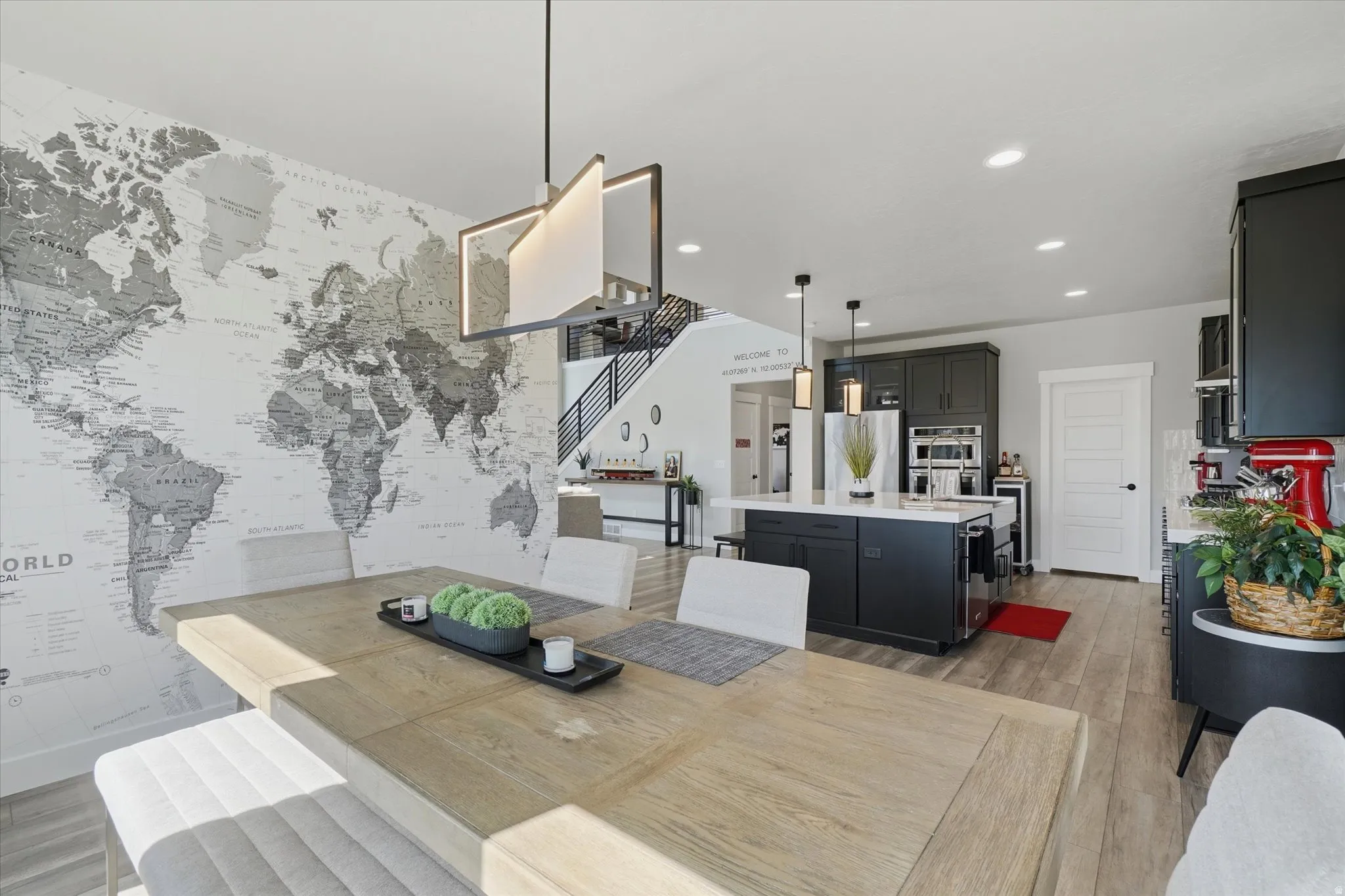 Open-concept dining area featuring a light wood-finish table, a decorative wall mural, and a contemporary chandelier