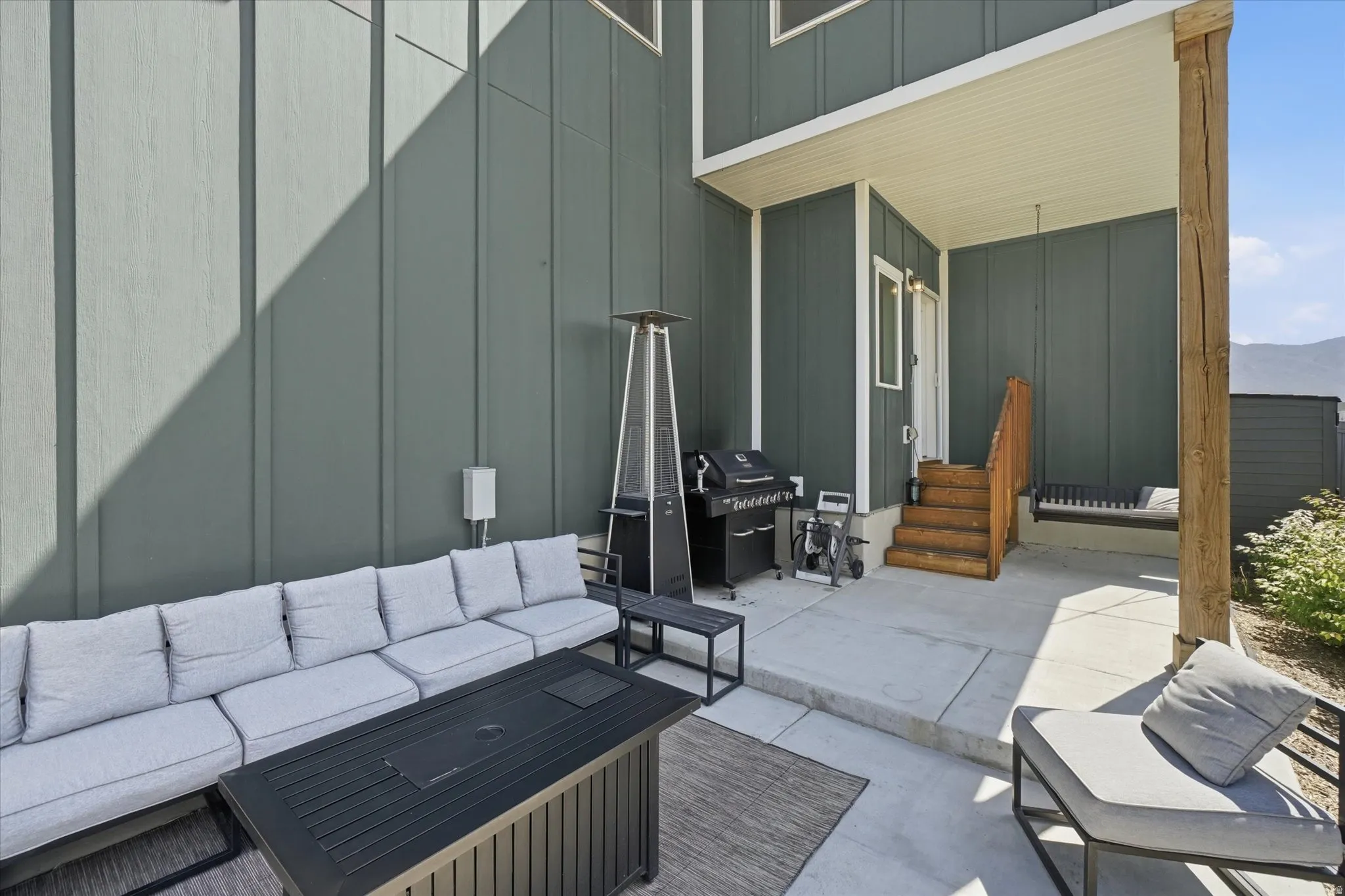 Concrete patio area featuring a covered porch, wood stairs with railing, and a built-in outdoor swing bench