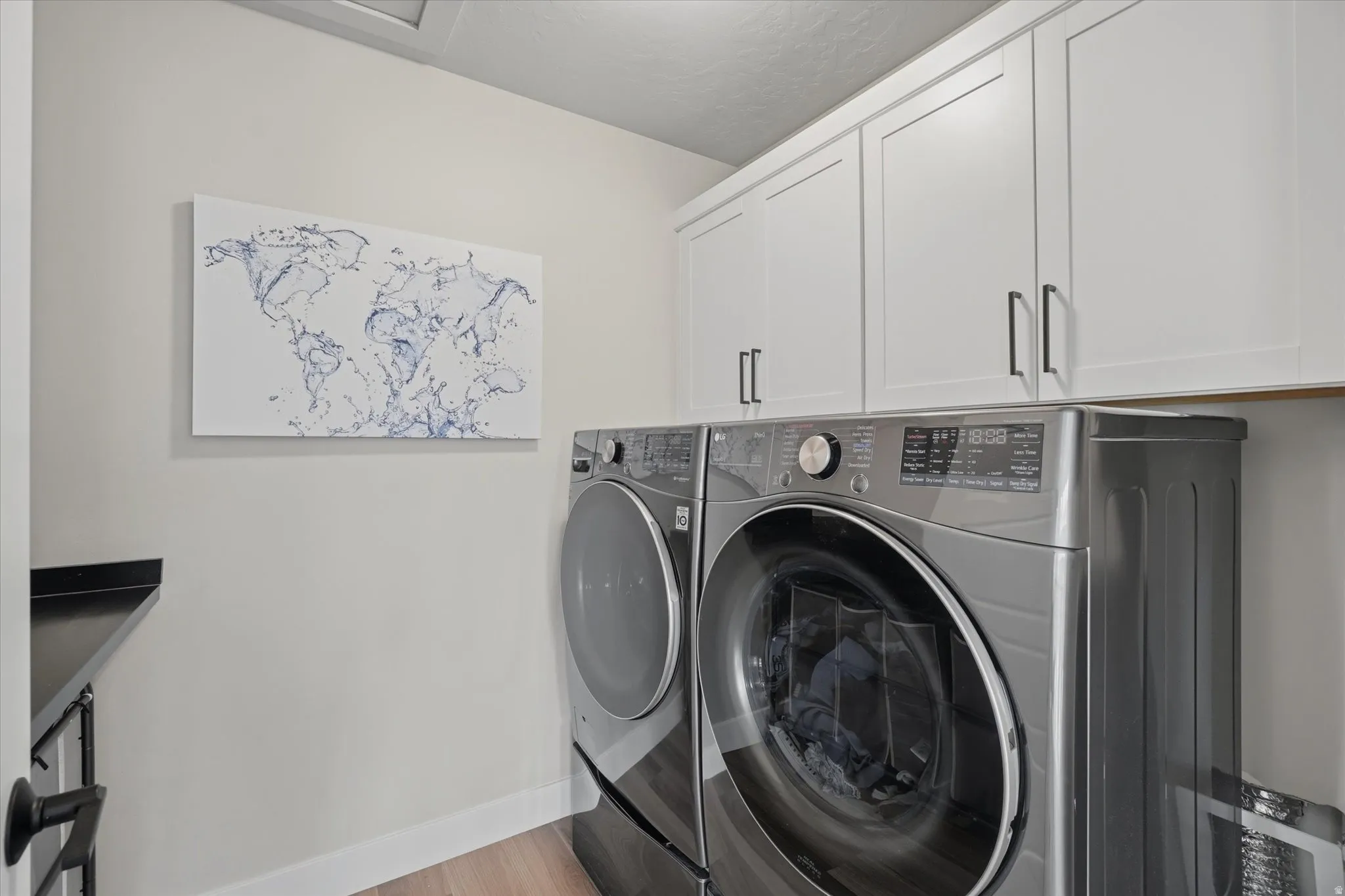 Dedicated laundry area featuring white shaker-style cabinetry with matte black hardware, a black countertop, and wood-finish flooring