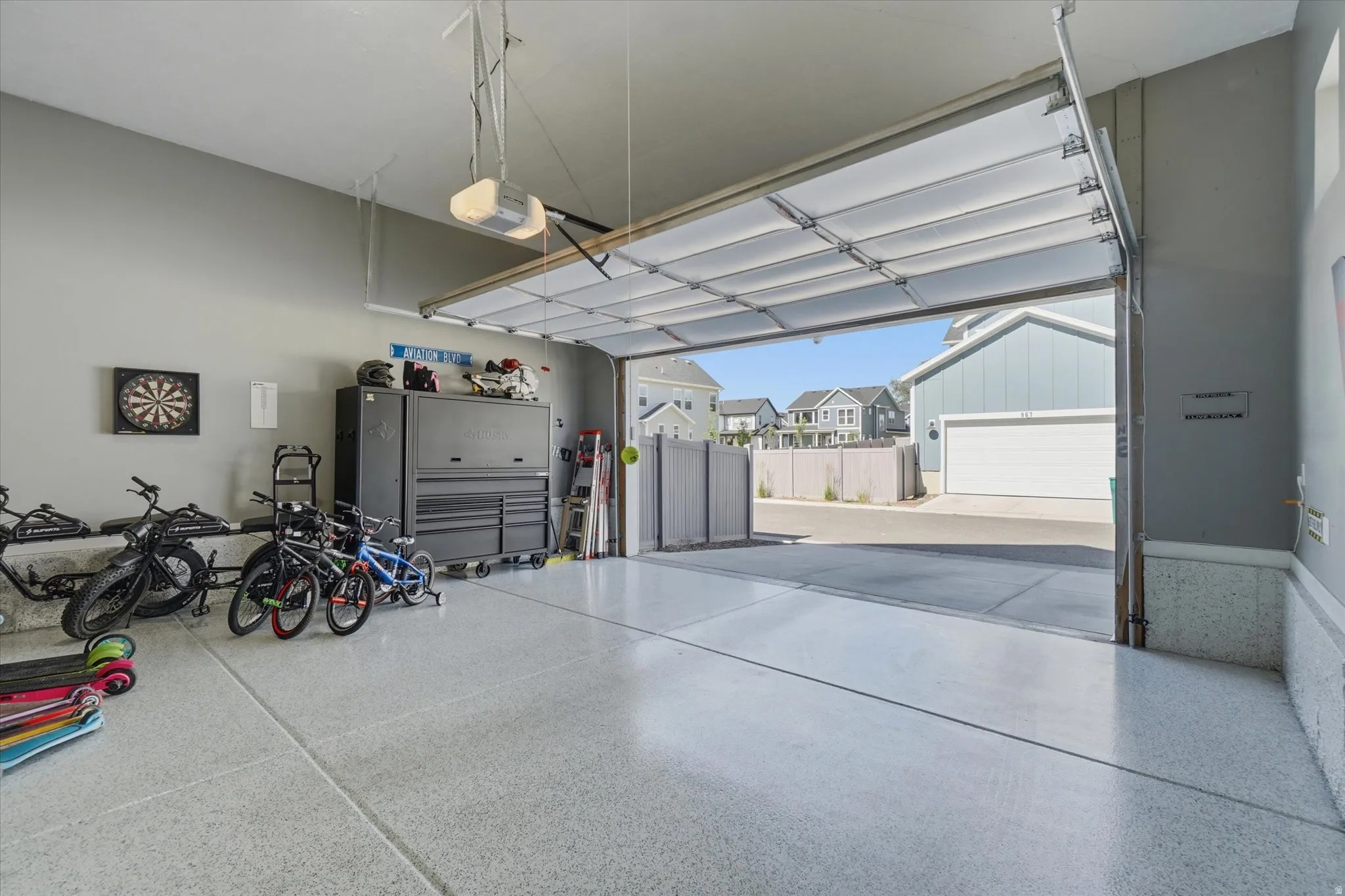 Spacious garage featuring an epoxy-coated concrete floor, neutral gray walls, an automatic garage door opener, and a clear overhead garage door providing ample natural light