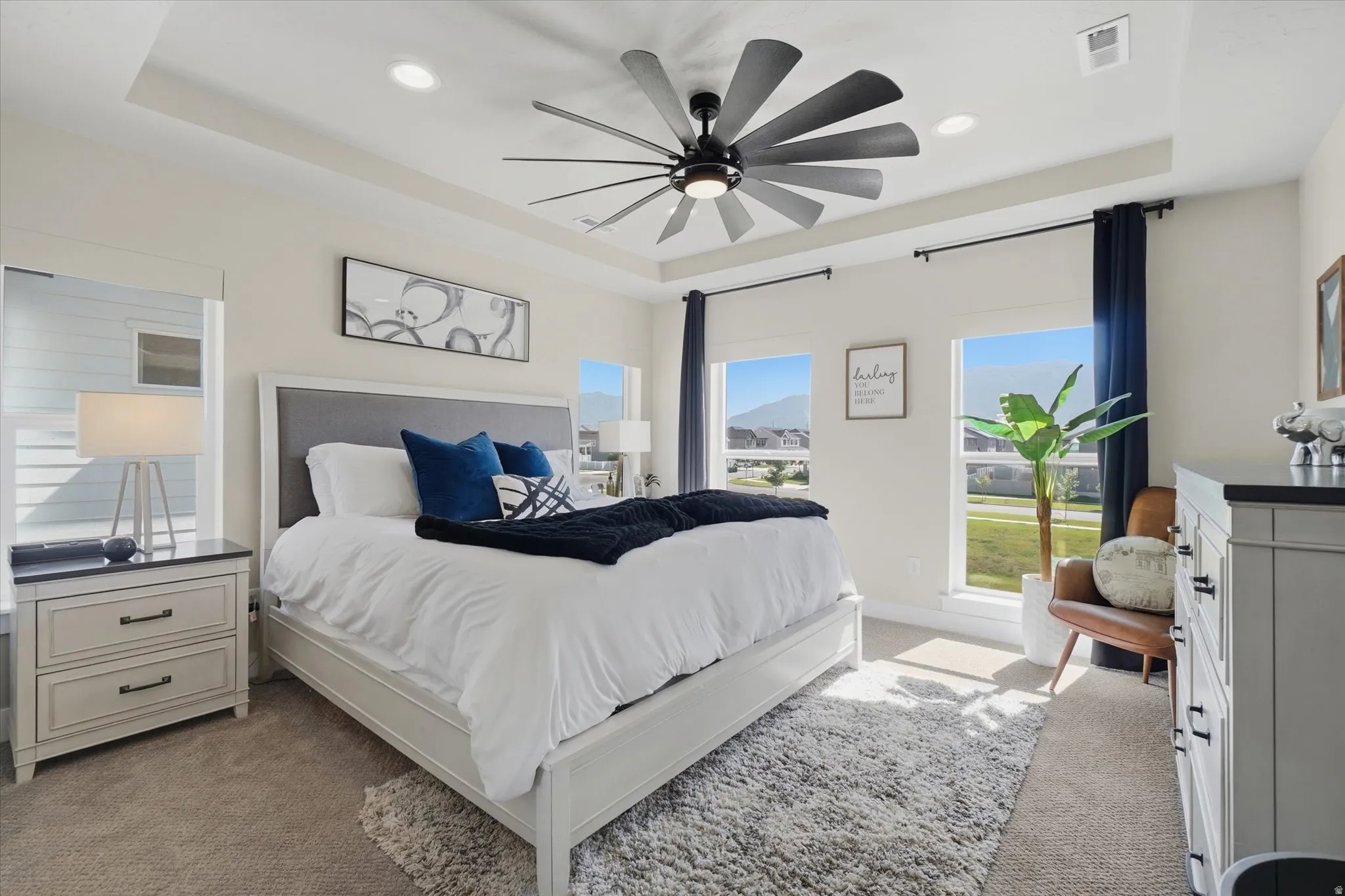 Spacious bedroom with a tray ceiling and recessed lighting, featuring carpet flooring and multiple windows