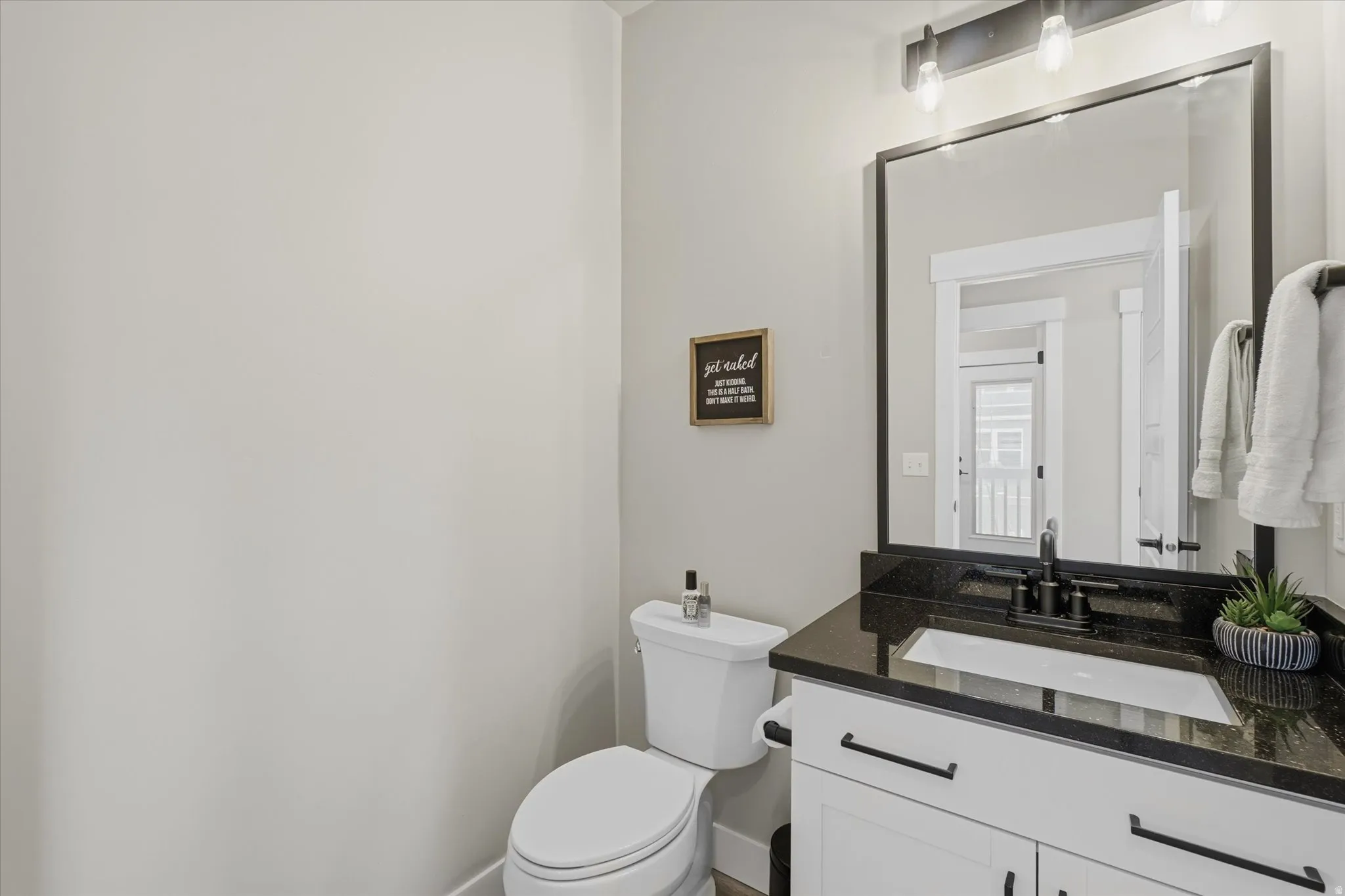Bathroom featuring a white vanity with black hardware, a black countertop, a rectangular undermount sink with a black faucet, and a large framed mirror with overhead lighting