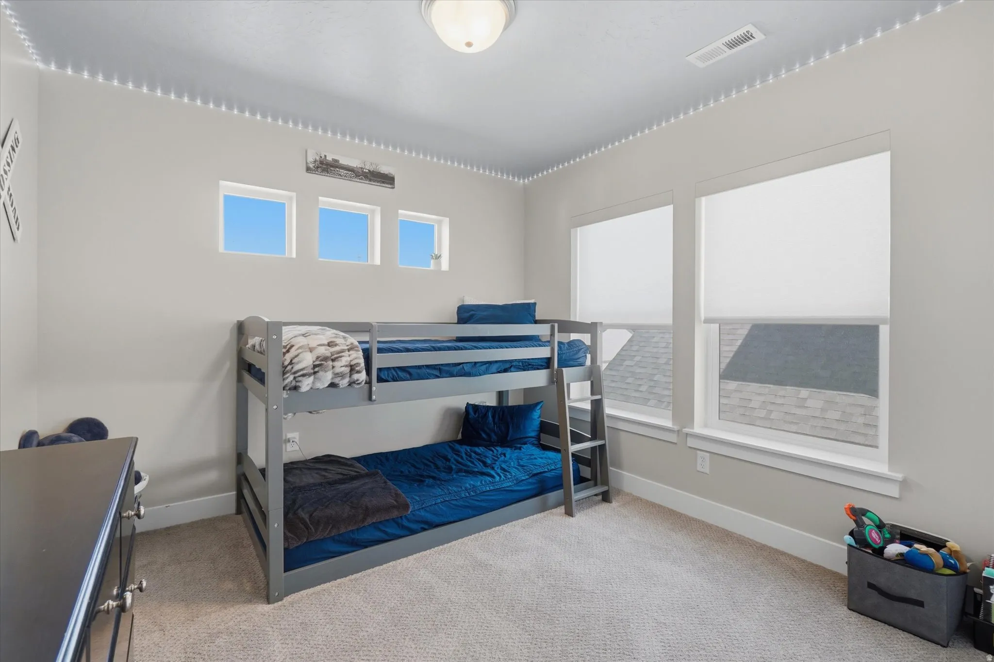 Carpeted room featuring a ceiling-mounted light fixture, multiple windows with roller shades, and a built-in air vent