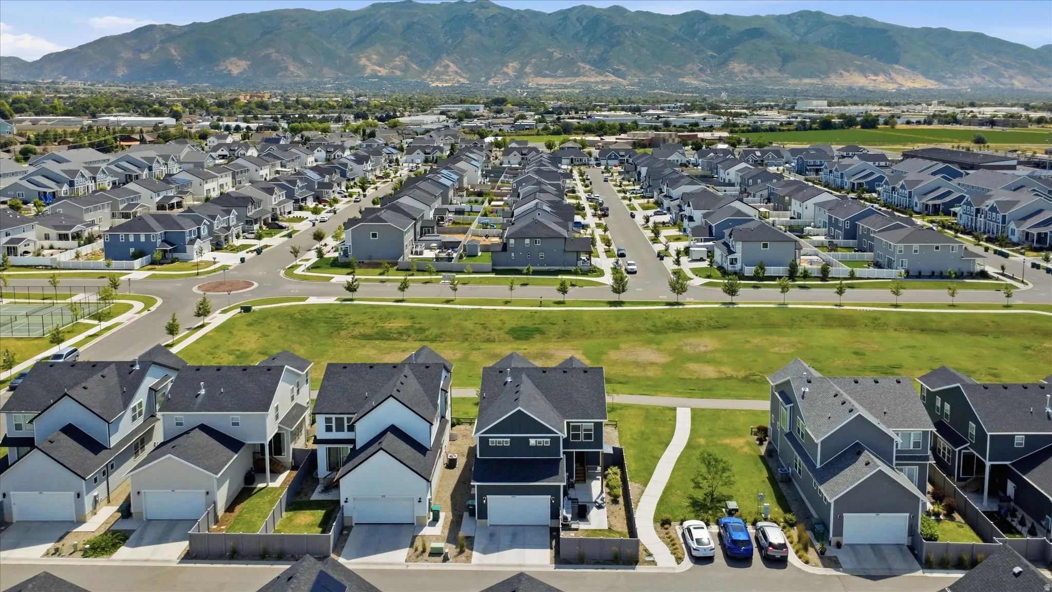 Expansive residential community featuring modern homes with dark roofs and light-colored siding, wide streets, and integrated green spaces
