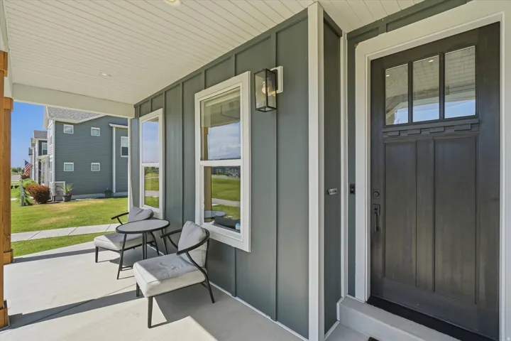 Front porch featuring a dark paneled entry door with upper window panes, board and batten siding, white window trim, and an exterior wall lantern
