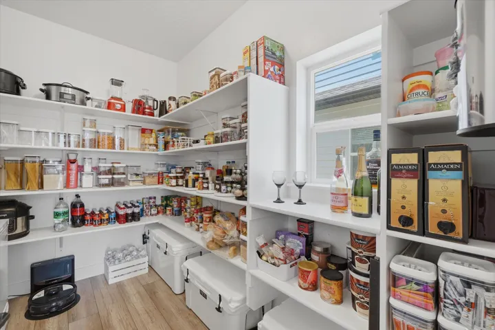 Spacious pantry featuring extensive built-in shelving, wood-finish flooring, and a window providing natural light