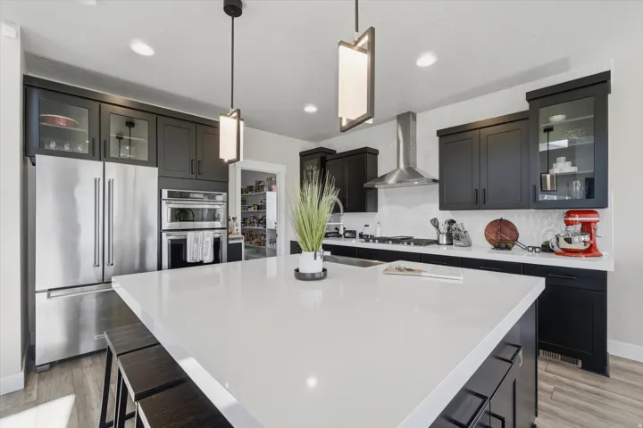Spacious kitchen featuring a large central island with a white solid surface countertop, dark wood-finish flooring, recessed lighting, and modern pendant fixtures