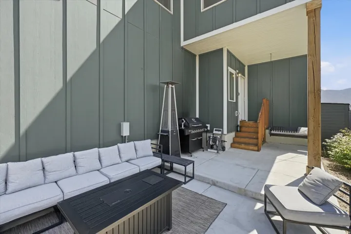 Concrete patio area featuring a covered porch, wood stairs with railing, and a built-in outdoor swing bench
