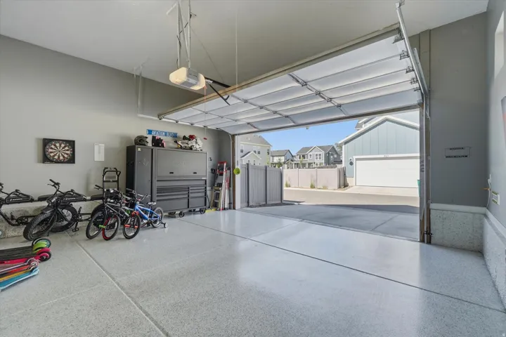 Spacious garage featuring an epoxy-coated concrete floor, neutral gray walls, an automatic garage door opener, and a clear overhead garage door providing ample natural light