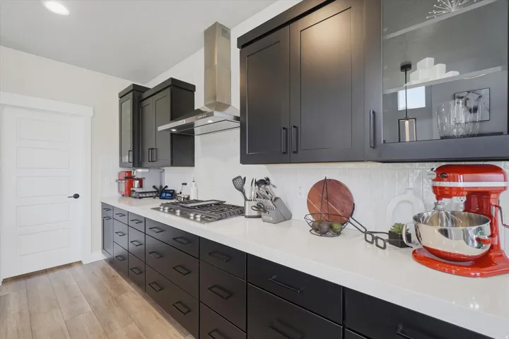 Contemporary kitchen featuring dark flat-panel cabinetry, a stainless steel range hood, white countertops, a gas cooktop, and a white subway tile backsplash
