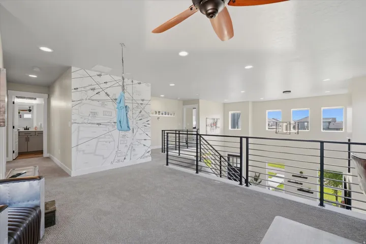 Spacious loft area featuring light gray carpeting, recessed lighting, a ceiling fan, and a contemporary metal railing overlooking the floor below