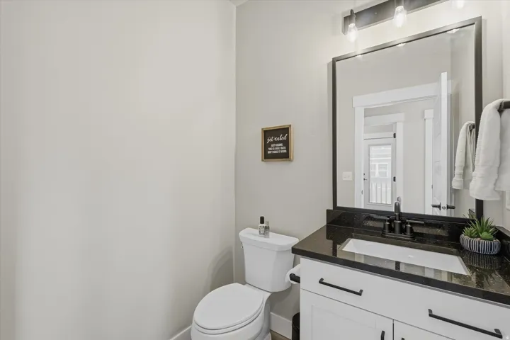 Bathroom featuring a white vanity with black hardware, a black countertop, a rectangular undermount sink with a black faucet, and a large framed mirror with overhead lighting