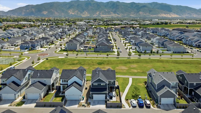 Expansive residential community featuring modern homes with dark roofs and light-colored siding, wide streets, and integrated green spaces