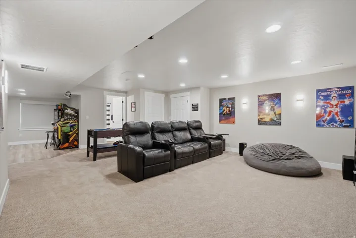 Spacious entertainment room featuring recessed lighting, wall-mounted sconces, and neutral-toned carpeting