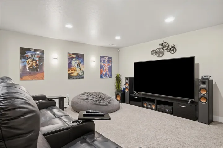 Carpeted entertainment space featuring a large wall-mounted television, recessed lighting, and built-in wall sconces