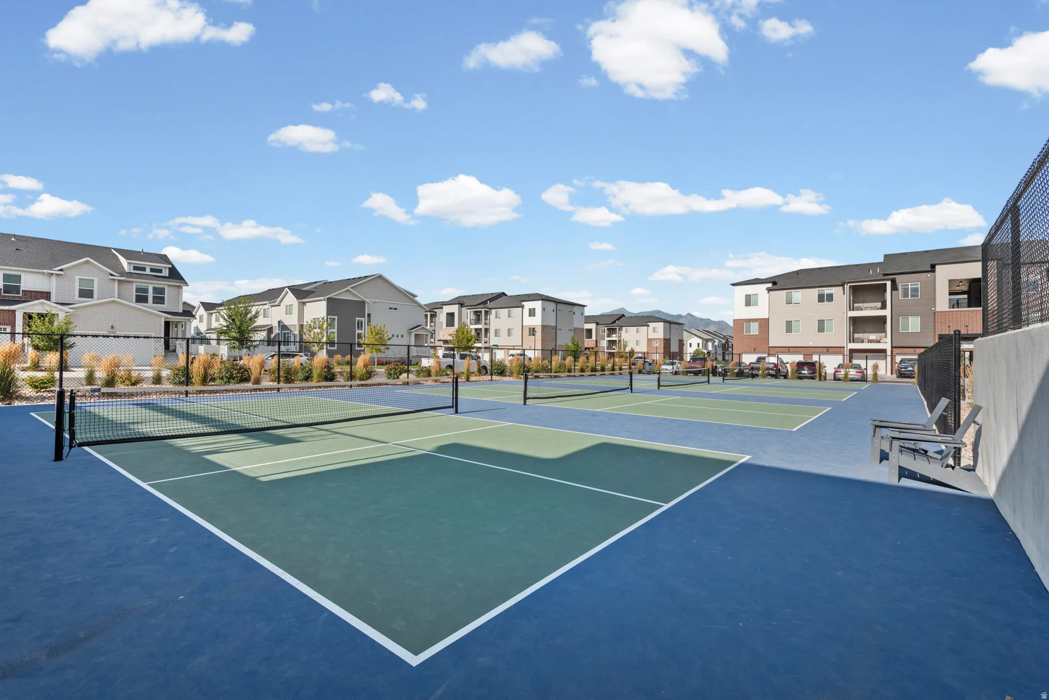Multiple blue and green hard-surface courts with nets, surrounded by decorative landscaping and perimeter fencing